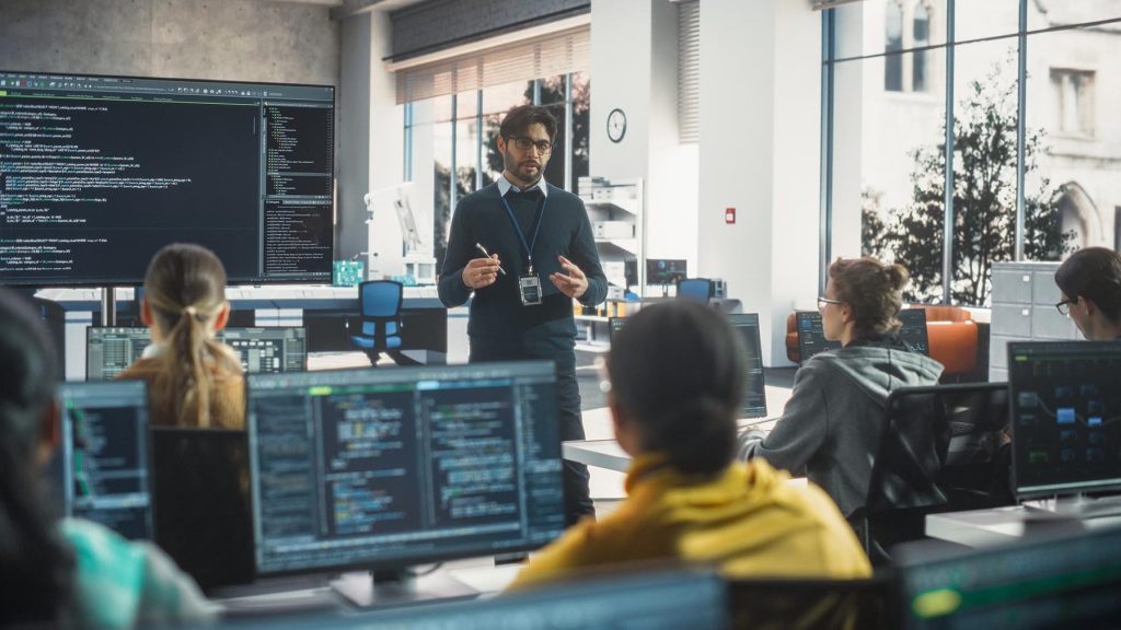 IT professional standing at front of room instructing students on writing programming code